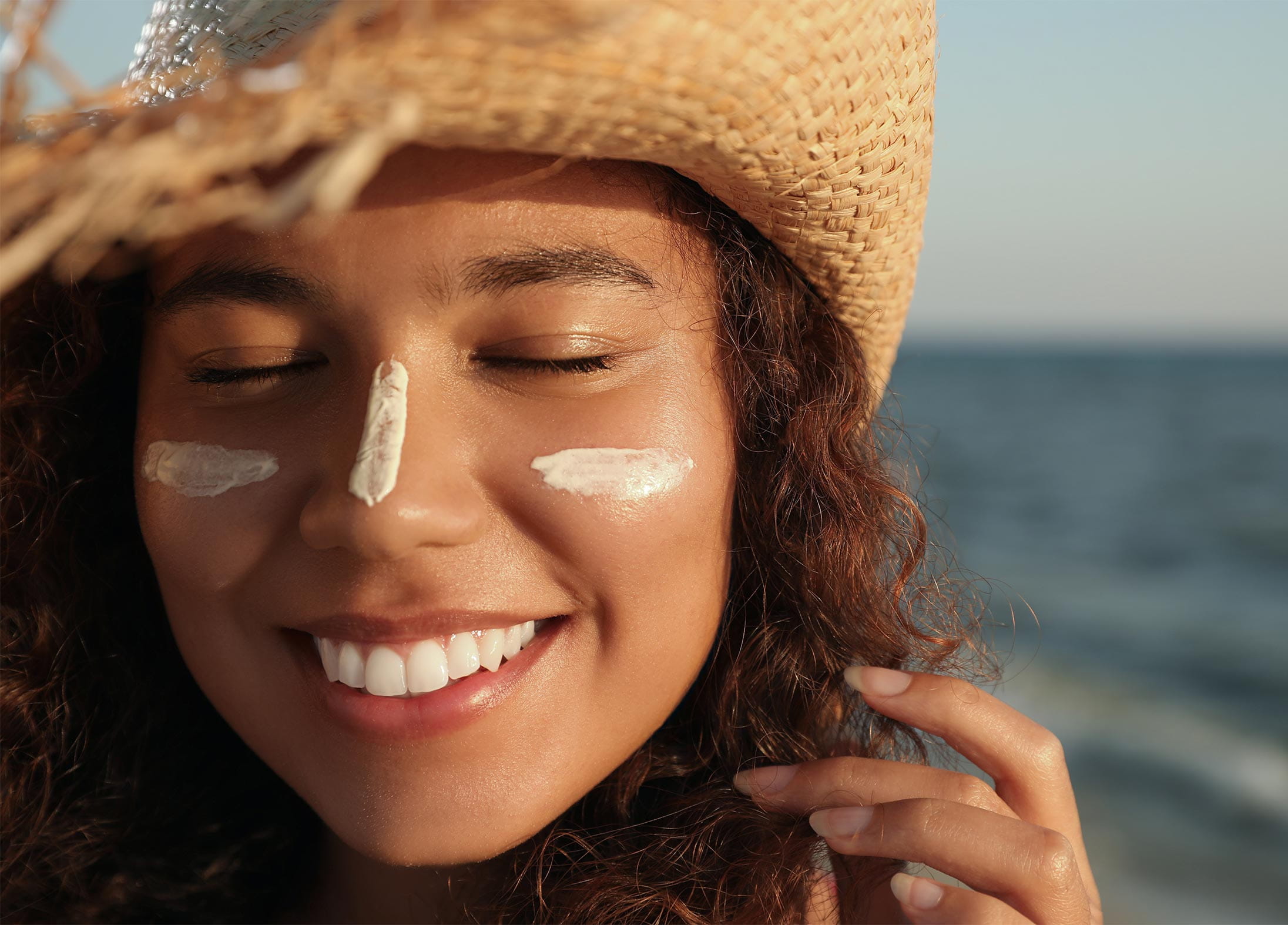 A woman smiling at the beach wearing sunscreen