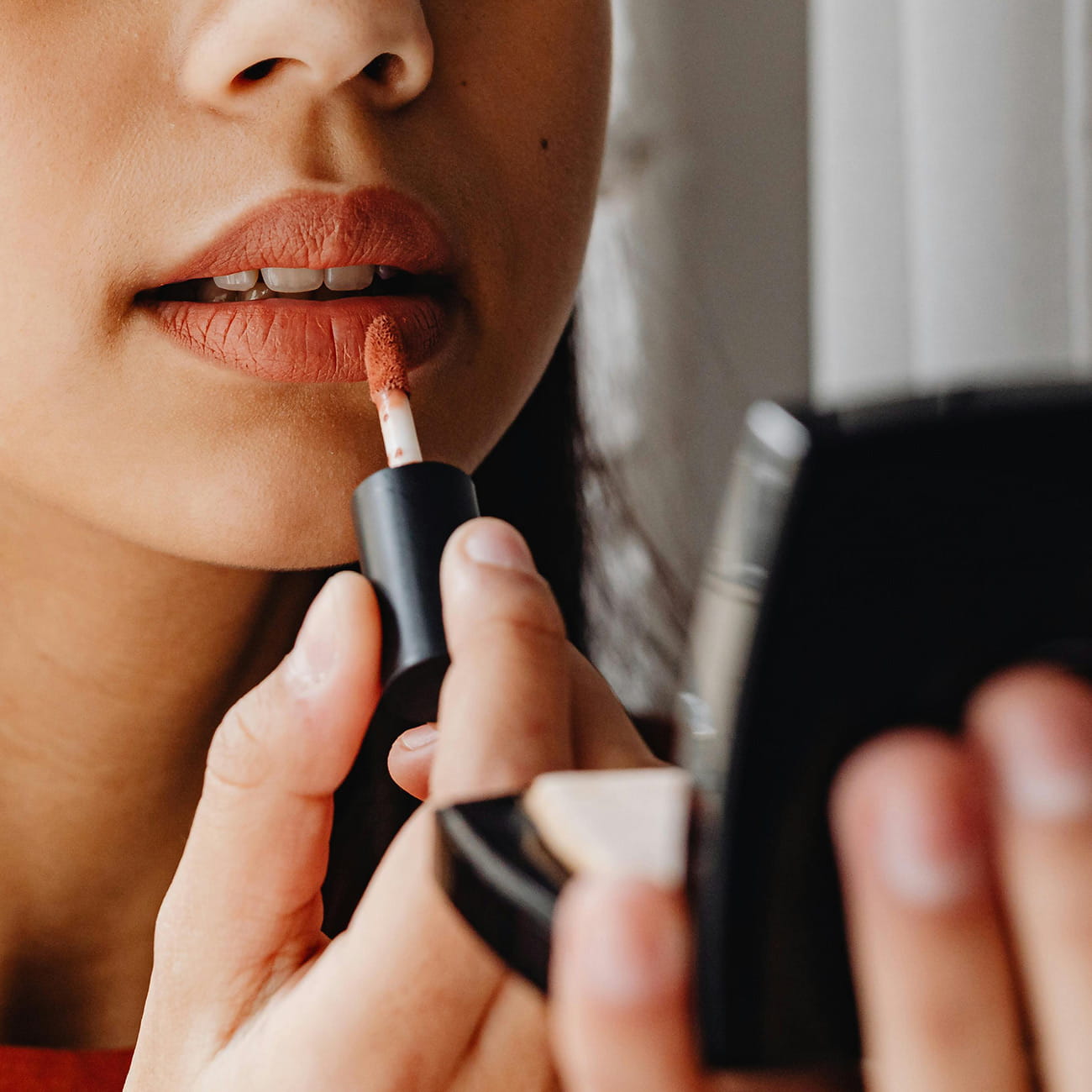 A woman applying lipstick with a compact